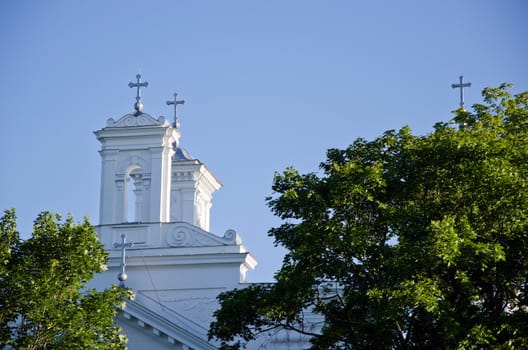 Church towers and cross visible through tree branches on background of blue sky. Religious catholic view.