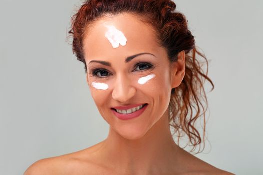 Beautiful natural middle aged woman cover face with cream isolated on grey background