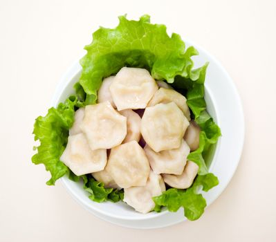 Russian hot pelmeni in a dish, close up. with sheet of the salad