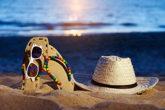 Wicker hat, sandal and glasses on the sandy beach