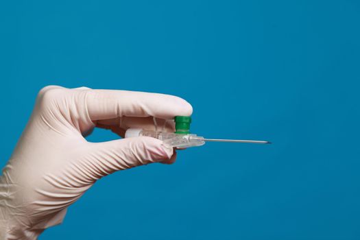 Hand in surgical glove holding a small intravenous needle against a blue background.