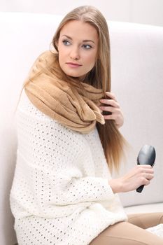 Smiling young woman combing her hair sitting on the sofa