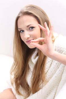 Young long-haired blonde sitting on a sofa. She holds a pill