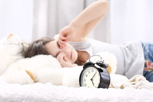 Girl sleeping on the bed. Rubs her eyes, an alarm clock in the foreground