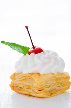 puff pastry cake with cream cherry and fresh mint leaf on white plate