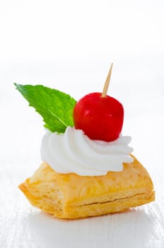 puff pastry cake with cream red marzipan ball and fresh mint leaf on white plate