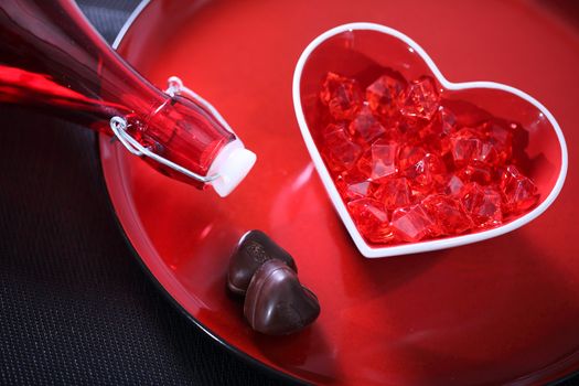 Red glass heart on a plate with bottle and chocolate