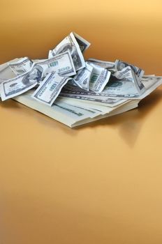 Stack of american dollars covered by small size one hundred fake banknotes. Golden background.