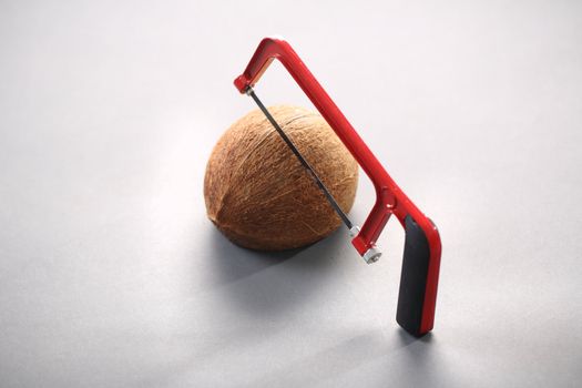 Coconut on white background crossed with a red saw