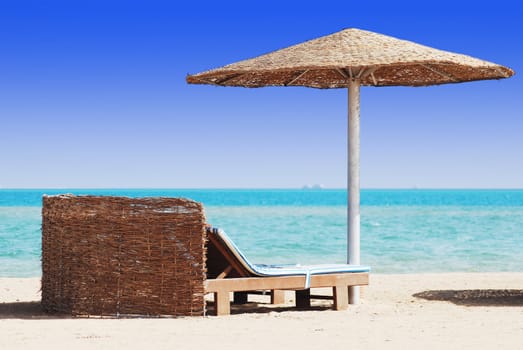 empty beach chair with straw sunshade at the sea