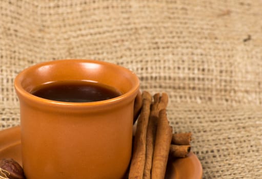 Coffee cup with cinnamon, coffe beans, nuts and lemon over sacking