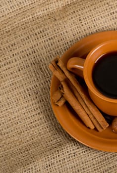 Closeup shot of freshly prepared cup of italian espresso with cinnamon, coffe beans, nuts and lemon over sacking
