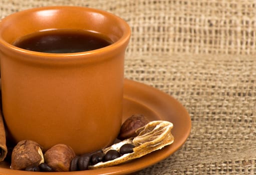 Coffee cup with cinnamon, coffe beans, nuts and lemon over sacking