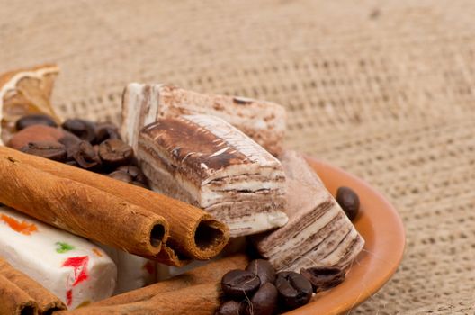 Sweets, cinnamon, nuts and coffee beans on a saucer, on burlap background.