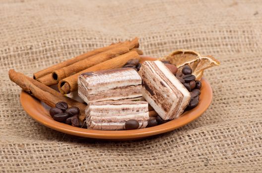 Sweets, cinnamon, nuts and coffee beans on a saucer, on burlap background.