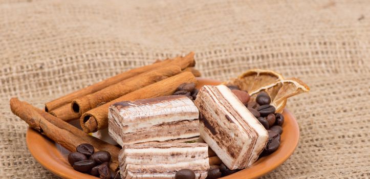 Sweets, cinnamon, nuts and coffee beans on a saucer, on burlap background.