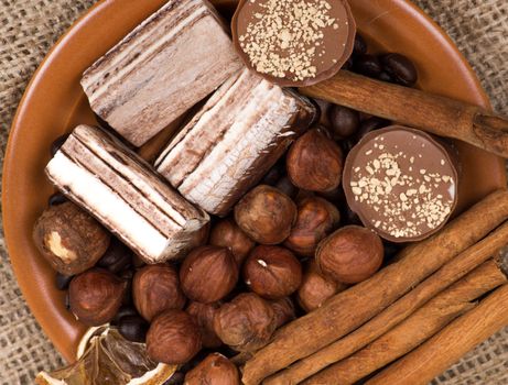 Sweets, cinnamon, nuts and coffee beans on a saucer, on burlap background.