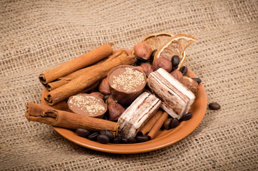 Sweets, cinnamon, nuts and coffee beans on a saucer, on burlap background.