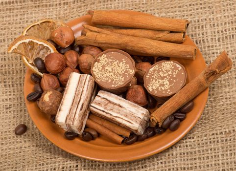 Sweets, cinnamon, nuts and coffee beans on a saucer, on burlap background.