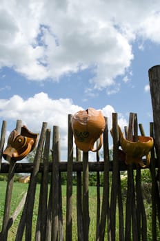 several clay broken pitchers hang on retro wooden fence from woven tree branches.