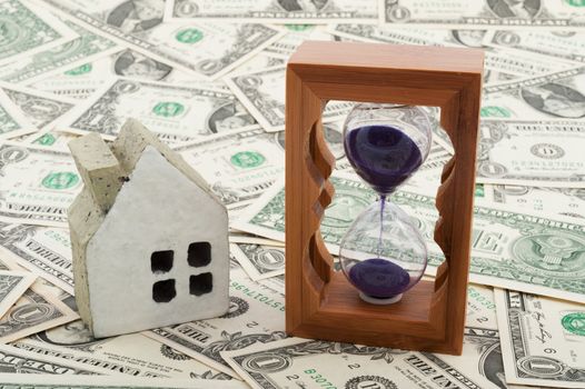 House model and hourglass on piles of paper money