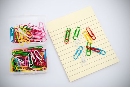 Colorful paper clips on pile of yellow paper against white background