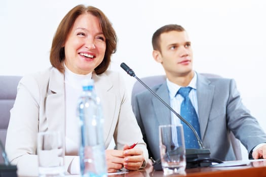 Image of two businesspeople sitting at table at conference speaking in microphone