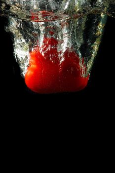 Colored red paprika in water splashes on black background