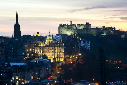 View of a floodlit Edinburgh Castle on the skyline at sunset with the lights of the city and illuminated landmarks in the foreground