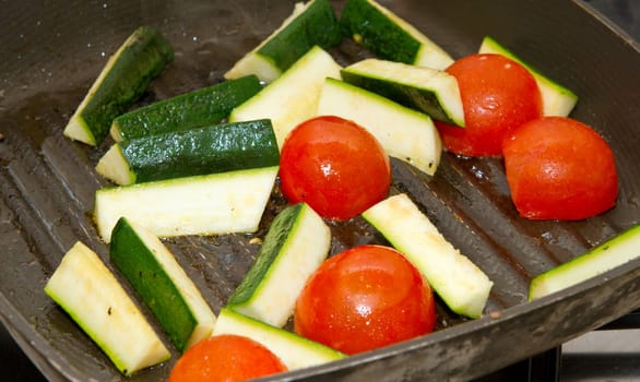 Aubergines and tomatoes frying in a griddle pan