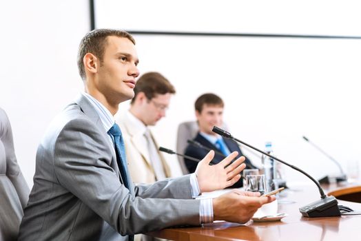 Portrait of a businessman, said into the microphone, in the background colleagues communicate with each other