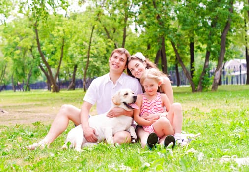 Happy young family with Labrador is resting in the park