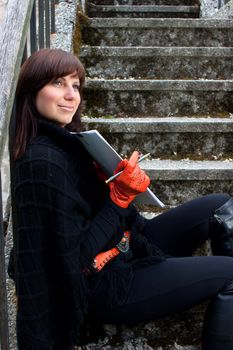 Beautiful smiling red gloved girl sitting on the stairs with drawing pad