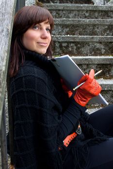 Beautiful smiling red gloved girl sitting on the stairs with drawing pad