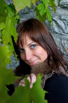 Beautiful blue-eyed smiling girl outdoors near the wall and maple