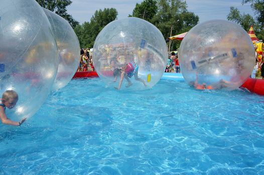 Children riding in a large zorb balls in the pool on a summer day.