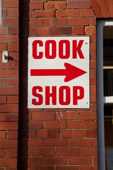 A red brick wall with a white sign and the words 'COOK SHOP' and an arrow written in red.