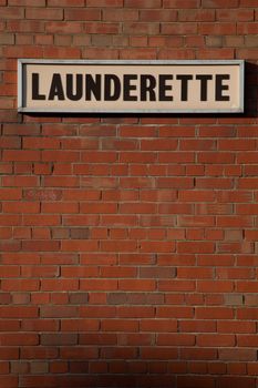 A red brick wall with a sign and the words 'LAUNDERETTE' written in black.