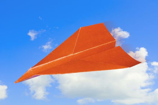 Red paper plane against sky with clouds.