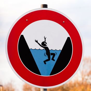 Circular hazard sign warning of danger of drowning with a pictorial illustration showing a person trapped by surroundings drowning in blue water