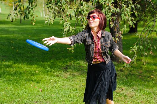 Young woman having fun with frisbee in the parkin sunny summer day.