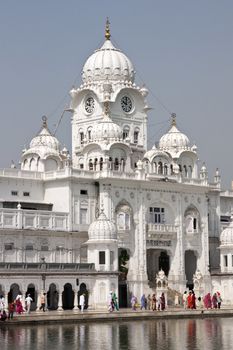 Golden Temple. Holiest shrine of the Sikh religion. Pilgrims walking in front of a white domed building by an artificial lake in Amritsar, Punjab, India.