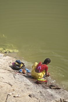 Indian lady squatting on a rock washing clothes in a lake in Chittaugarh, Rajasthan, India.