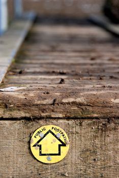 Yellow public footpath sign, leading across a muddy wooden walkway.