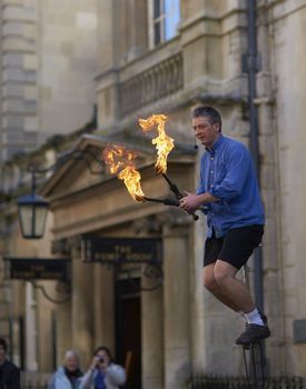 Street artist entertaining the crowds by juggling flaming torches whilst riding a unicycle in Bath, Somerset, England.