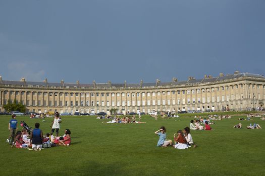 Groups of people enjoying the sunshine on the grass in front of the Royal Crescent in Bath, Somerset, England.