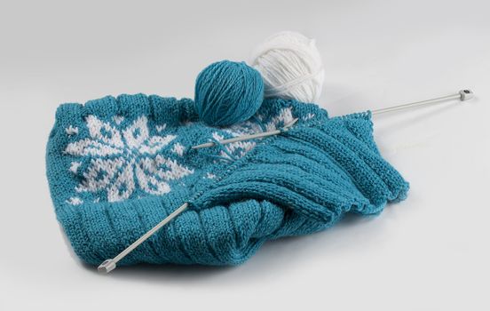 Turquoise knitting with clews and knitting needles on the grey background