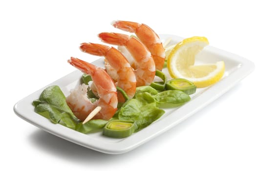 Four shrimp's tails on the skewer whit fresh lettuce, leek and lemon on the plate