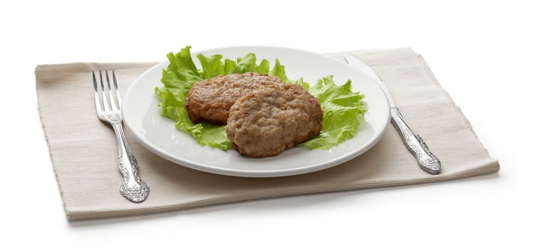 White plate with two rissoles and lettuce on the napkin with fork and knife