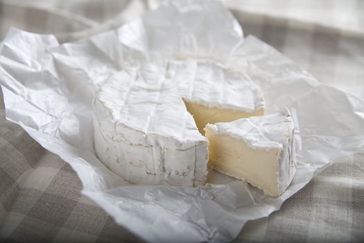 Camembert cheese on the white paper on the tablecloth